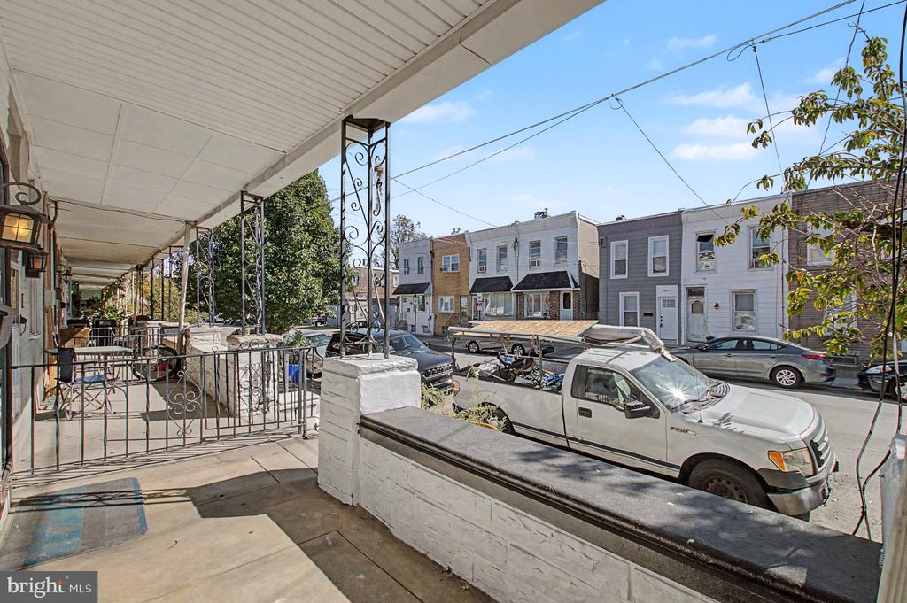 Covered front porch overlooking a Philadelphia residential street lined with rowhouses and parked cars.