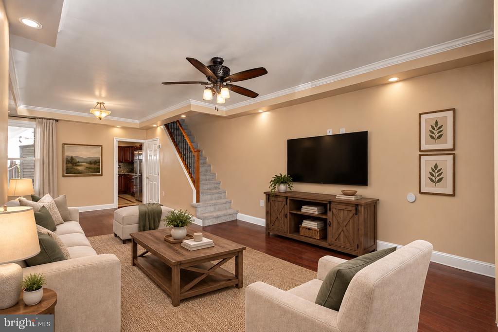 Staged living room with a carpeted staircase, cream sofas, and a wall-mounted television.