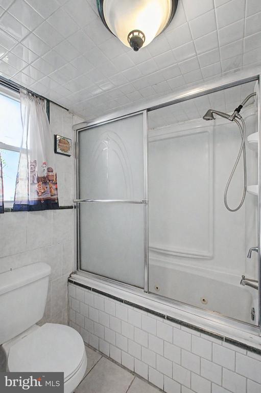 Bathroom with a tub-shower behind sliding frosted-glass doors and a curtained window.