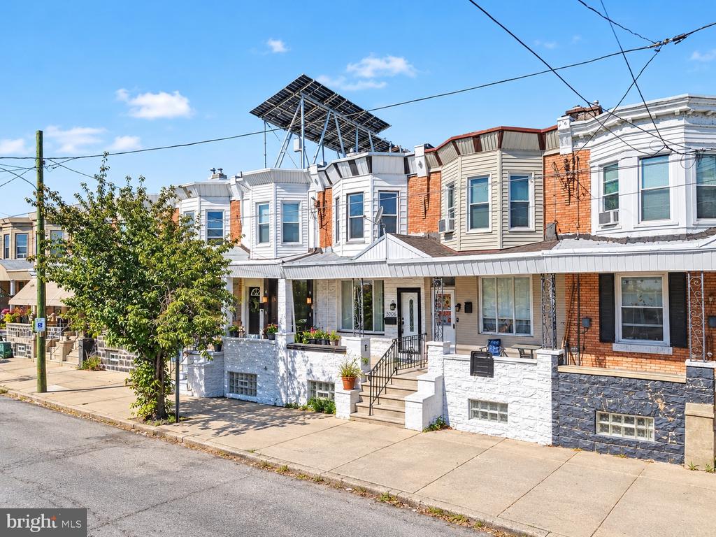 Philadelphia row house with a stone foundation, front porch, and rooftop solar panel array.