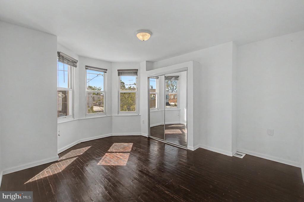 Empty bedroom with dark hardwood floors, bay windows, and mirrored sliding closet doors.