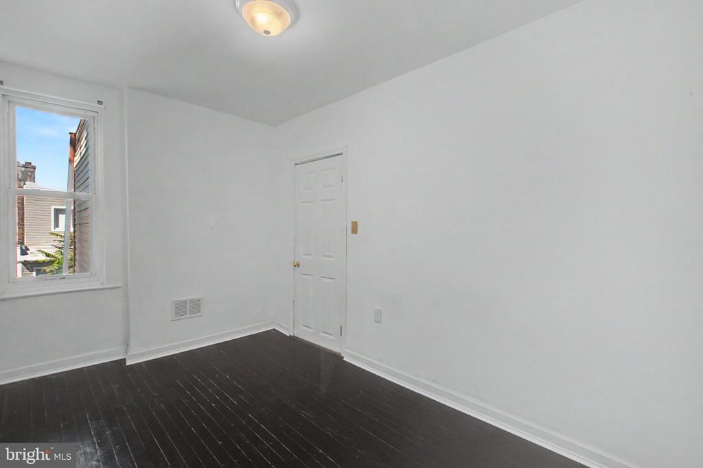 Empty room with dark hardwood flooring, white walls, and a window.