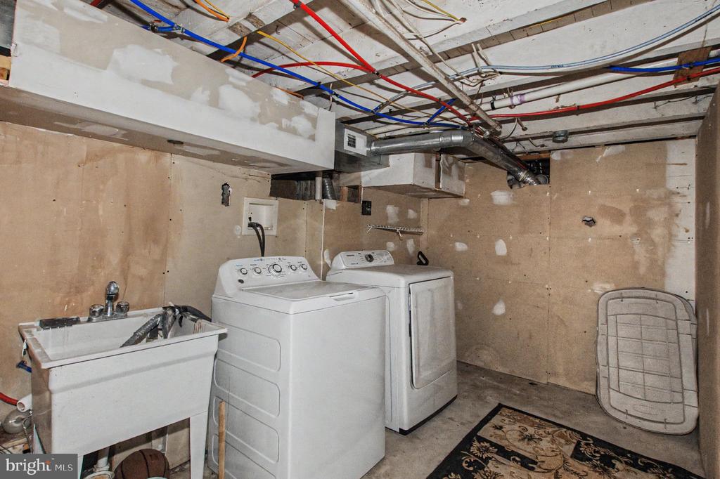 Basement laundry area with a utility sink, washer, and dryer beneath exposed wiring and ductwork.