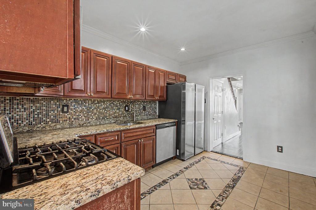 Kitchen with reddish-brown cabinets, granite counters, mosaic backsplash, and diagonal tile flooring.