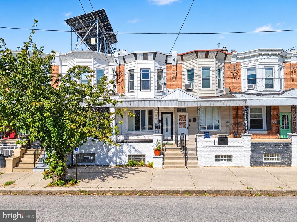 Rowhouse facade with a white porch, brick neighbors, and rooftop solar panels.