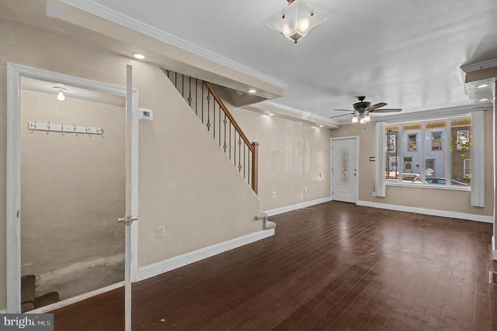 Empty living room with dark wood floors, a staircase, and a large front window.