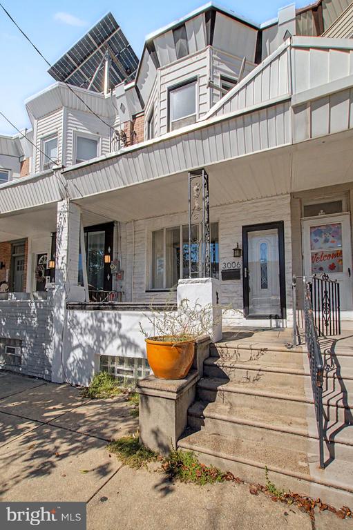 White-sided row house with a covered porch, front steps, black railing, and an orange planter.