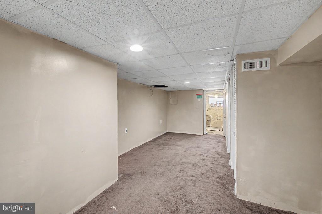 Empty basement room with brown carpet, beige walls, and a suspended tile ceiling.