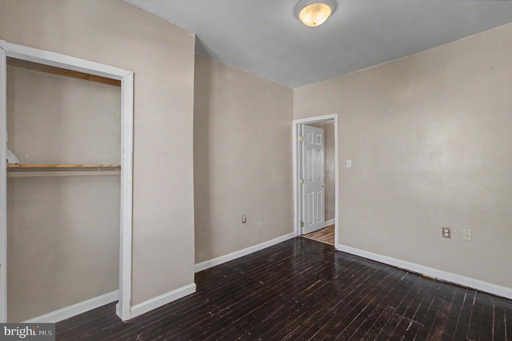 Empty bedroom with dark hardwood floors, an open closet, and a doorway to the hall.