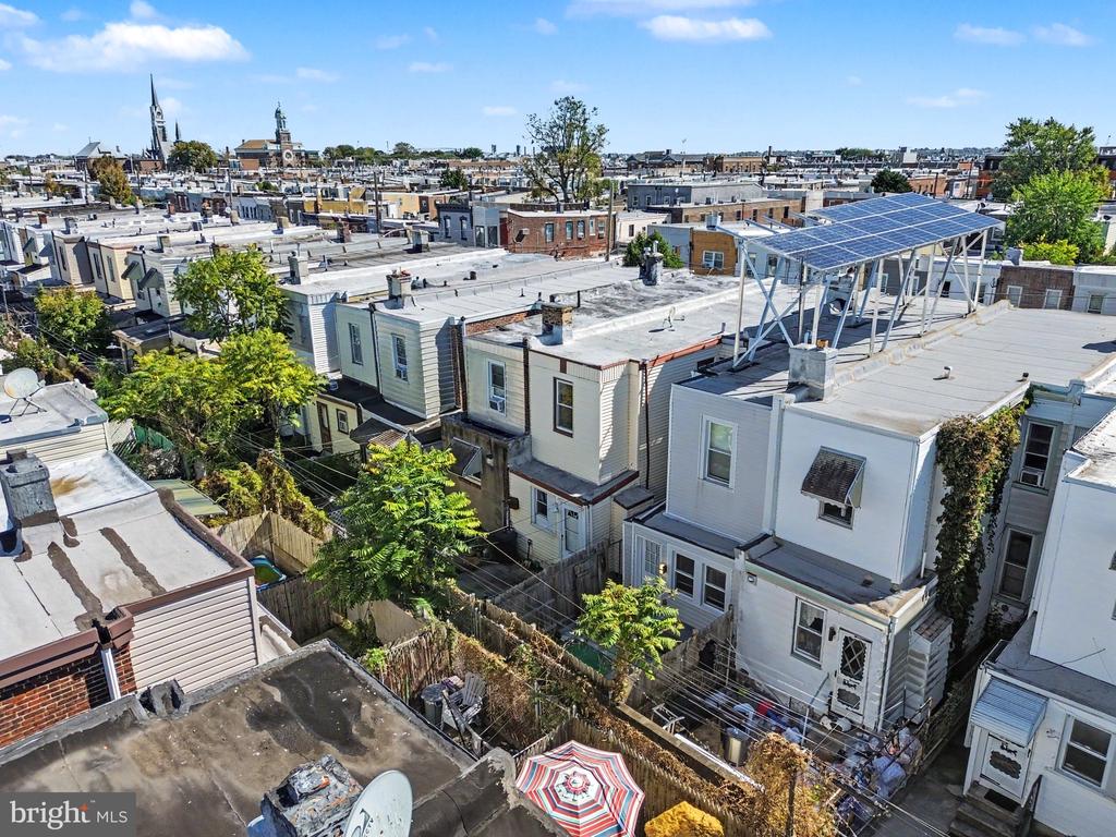 Aerial view of Philadelphia rowhomes and backyards, with rooftop solar panels and church steeples in the distance.