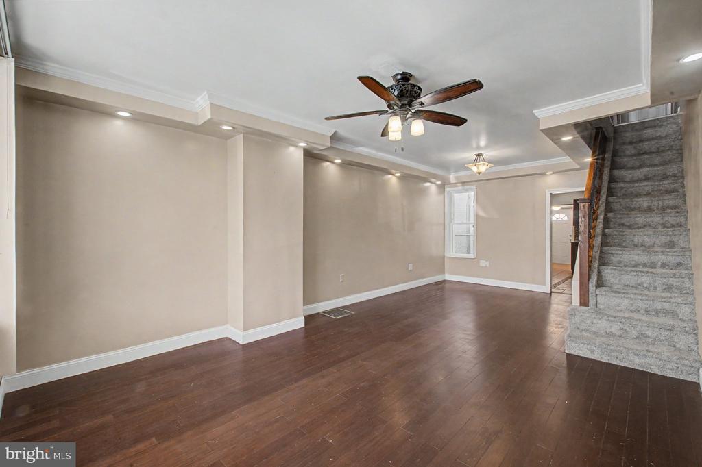Unfurnished living room with dark hardwood floors and a carpeted staircase.