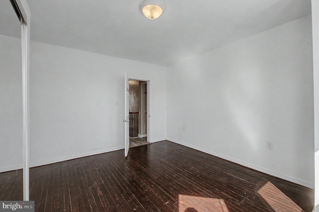Empty room with dark hardwood floors, white walls, and an open doorway to the hall.