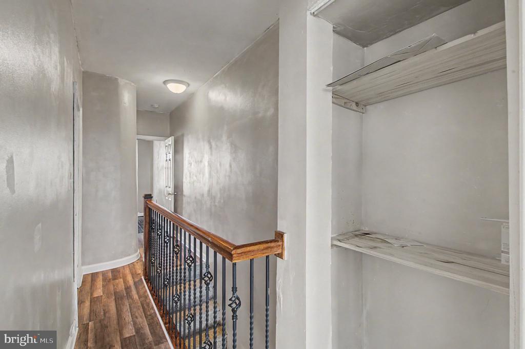 Hallway landing with wood-look flooring, a metal-and-wood railing, and an open shelved closet.