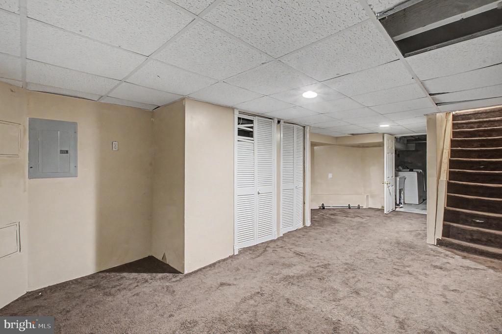 Vacant basement with louvered storage doors, carpeted floor, and stairs.