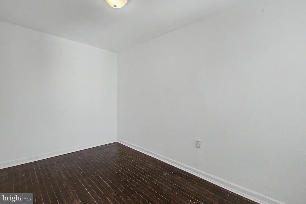 Empty room with dark hardwood floors, white walls, and a ceiling light.