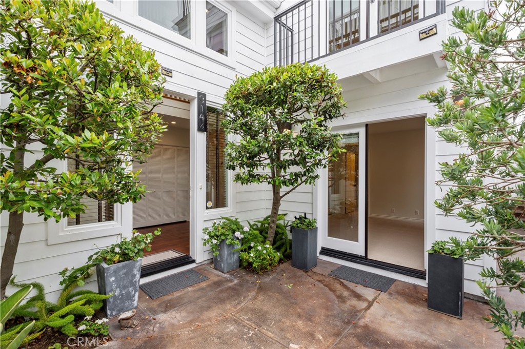 White-sided home entrance with glass doors, potted trees, and a planted courtyard.