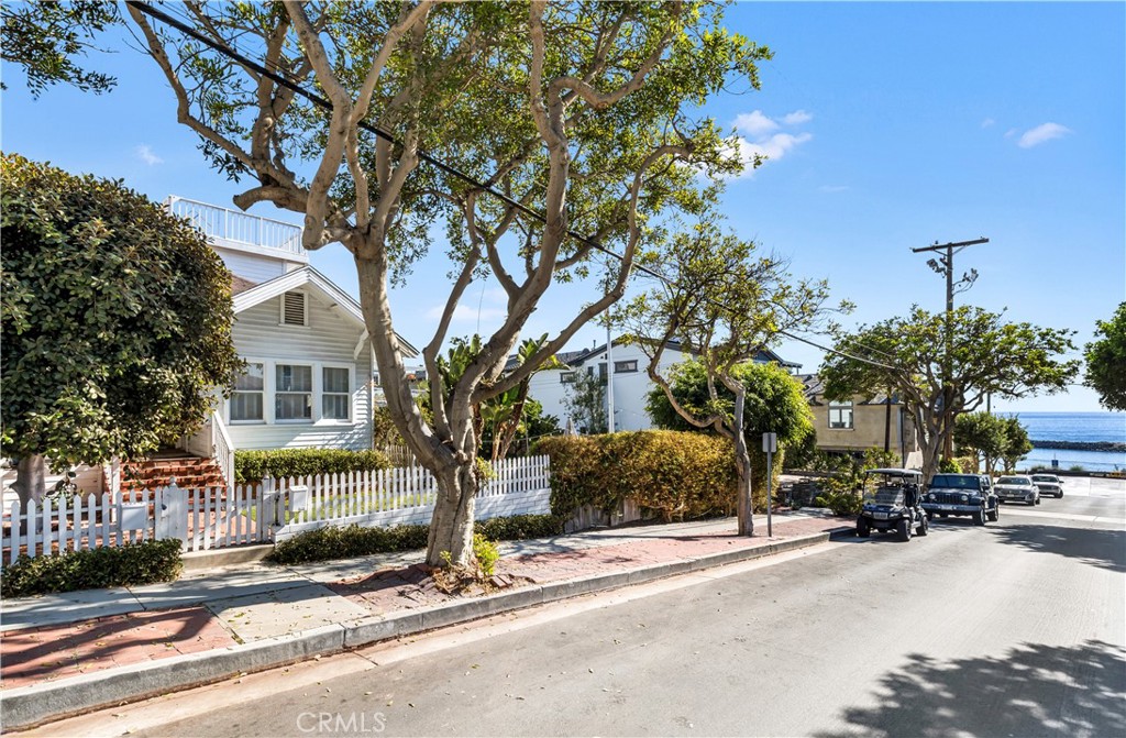 White coastal house behind a picket fence, with the ocean visible at the end of the street.