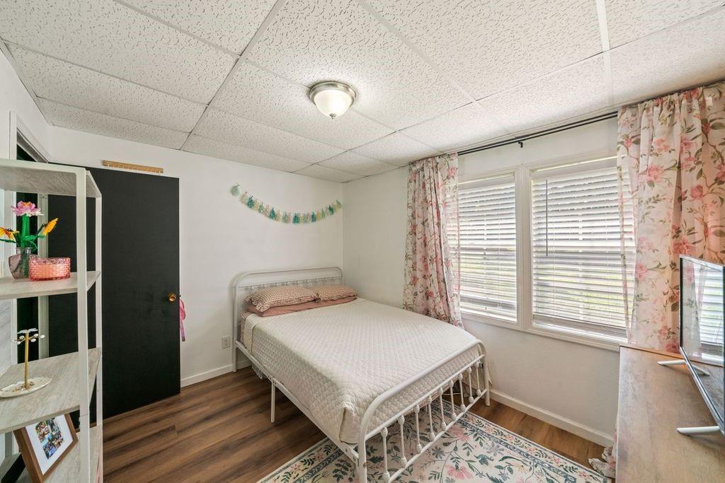 Bedroom with a white metal bed, floral curtains, and a large window with blinds.