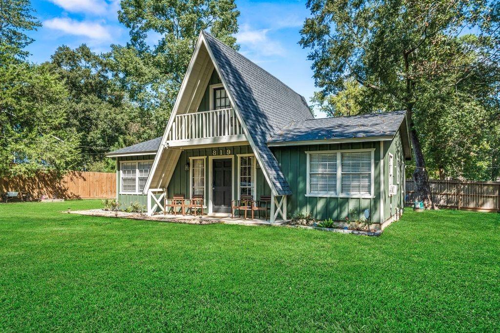Green A-frame house with a steep roof, front porch, and expansive lawn.