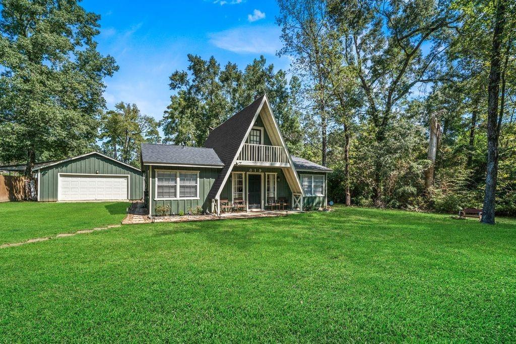 A-frame home with green siding, a detached garage, and a broad lawn.