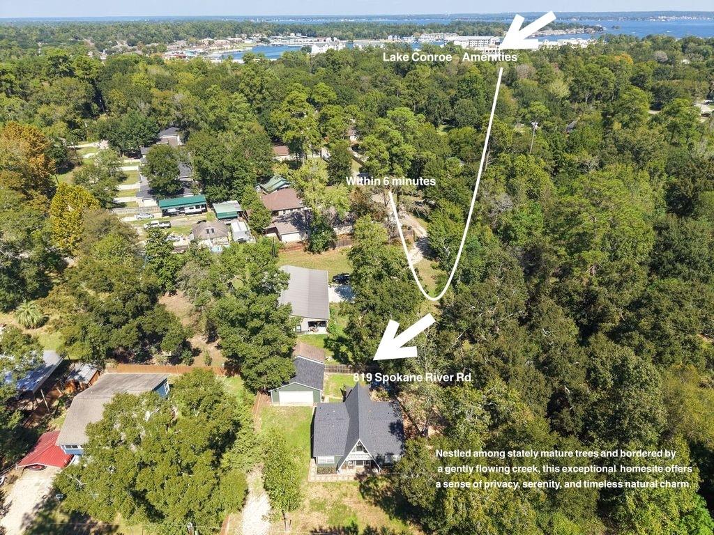 Aerial view of 819 Spokane River Road among mature trees, with Lake Conroe visible in the distance.