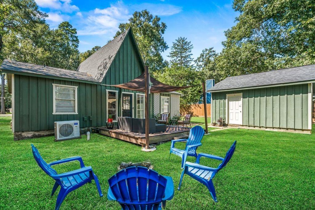 Green home with a shaded deck, detached shed, and blue Adirondack chairs on the lawn.