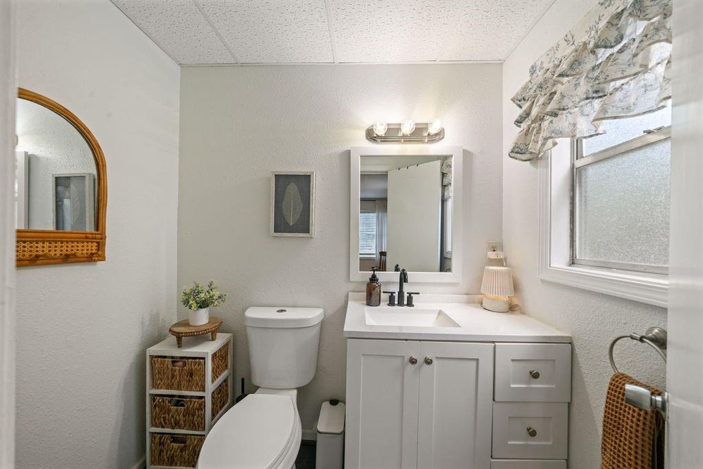 Bathroom with a white vanity and sink, toilet, framed mirror, and a window with a patterned valance.