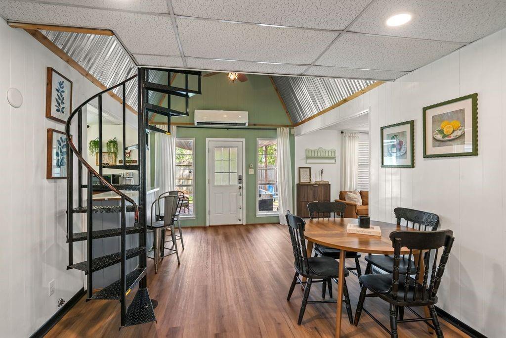 Dining area with a spiral staircase, wood floors, and a high metal ceiling.
