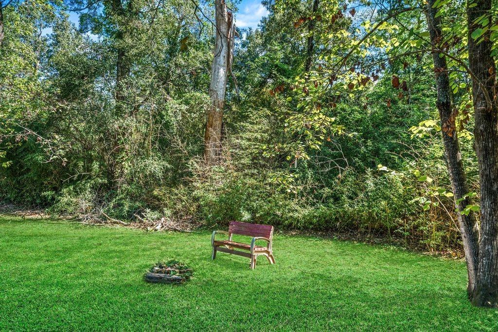 Wooded backyard with a grassy lawn, wooden bench, and small stone fire pit.