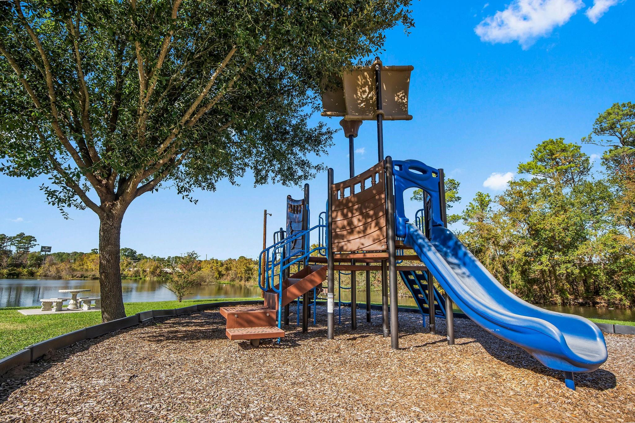 Playground with blue slides beside a pond and shaded picnic area.