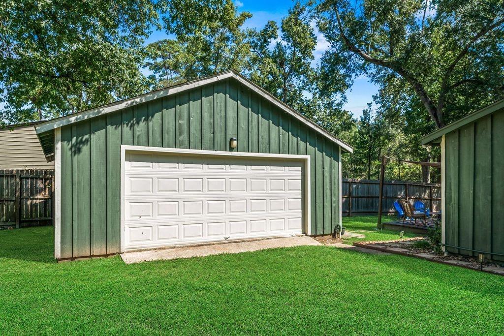 Detached green garage with a white double door, lawn, and mature trees.
