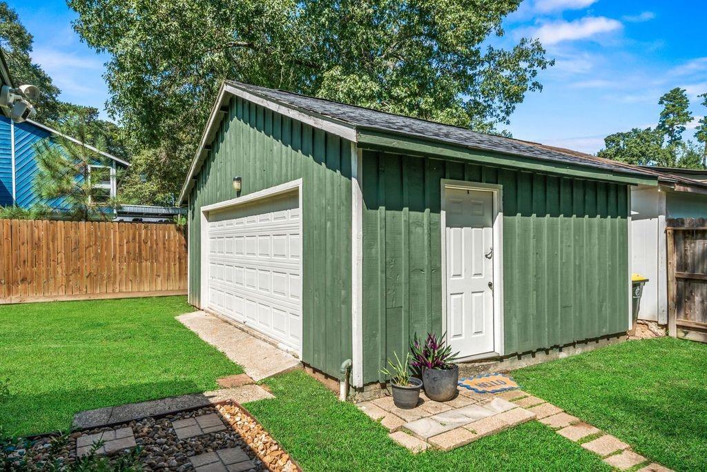 Green detached garage with a white overhead door and side entrance, surrounded by lawn.
