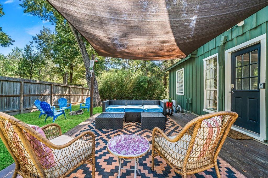 Shaded backyard deck with wicker chairs, a blue outdoor sofa, and a patterned rug.