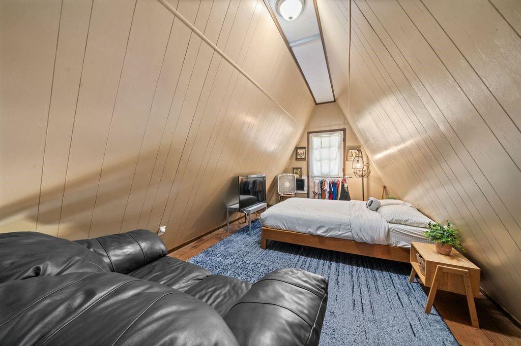 Attic bedroom with a bed beneath sloped wood-paneled walls and a black leather sofa.