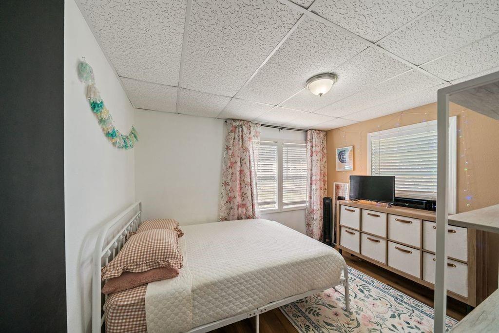 Bedroom with a white bed, floral curtains, and a dresser beneath wide windows.