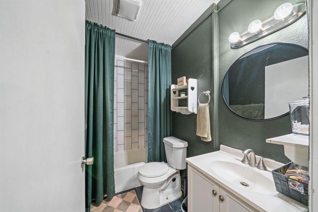 Bathroom with a tiled tub and shower, teal curtains, and a white vanity beneath an oval mirror.
