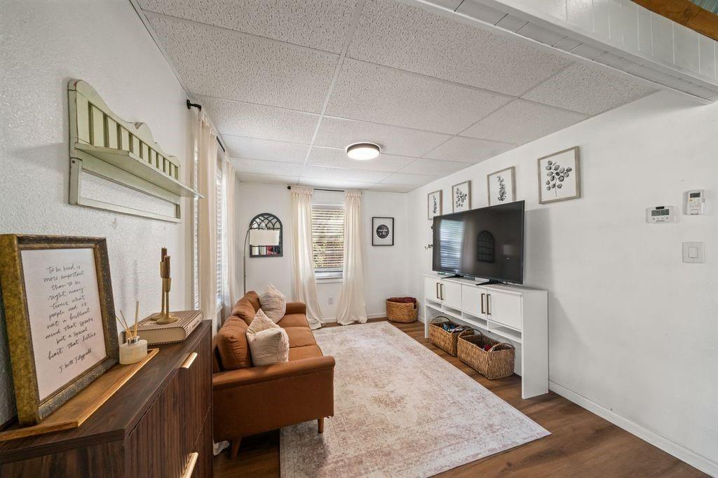Living room with a caramel sofa, pale area rug, and TV on a white console.