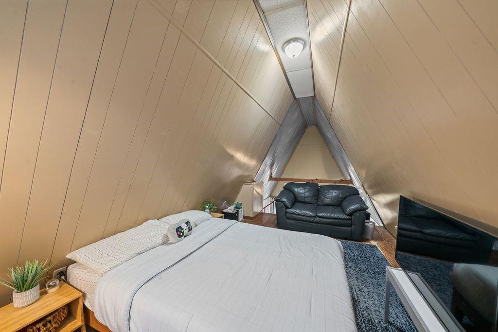 Loft bedroom with a large bed, black leather sofa, and sloped wood-paneled ceiling.