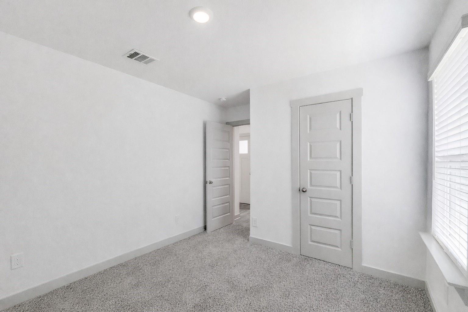 Empty bedroom with gray carpet, white walls, and a window with blinds.