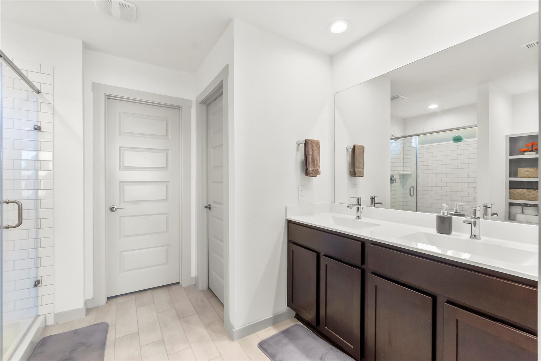 Bathroom with a dark double vanity and a glass-enclosed subway-tile shower.
