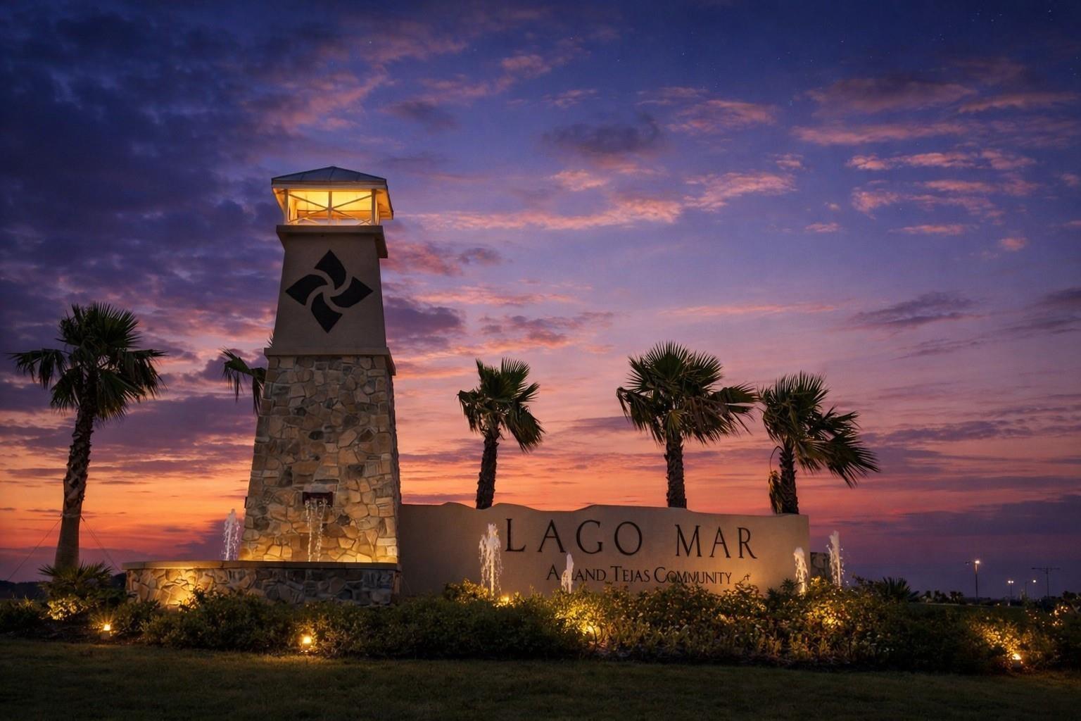 Lago Mar community entrance monument with a lit stone tower and palm trees at dusk.
