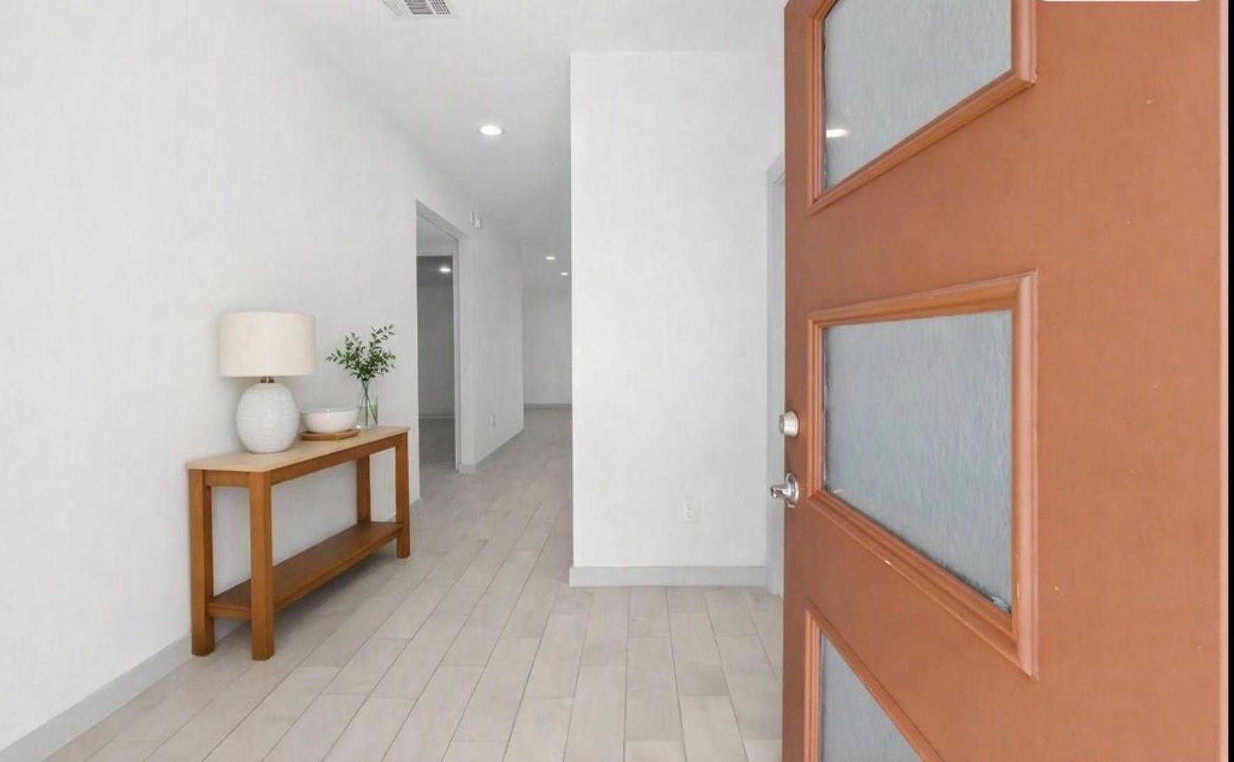 Entry foyer with light tile flooring, an open wood-and-frosted-glass door, and a decorated console table.