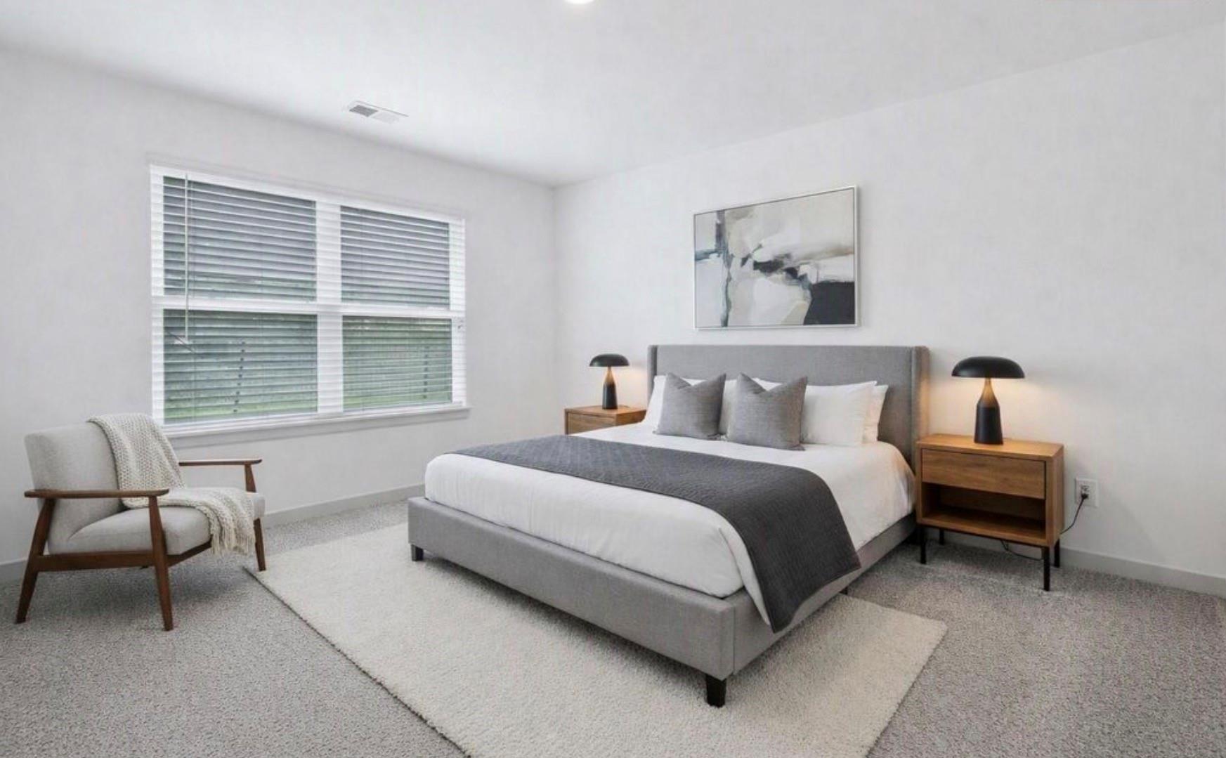 Furnished bedroom with a gray upholstered bed, matching nightstands, and a window with white blinds.