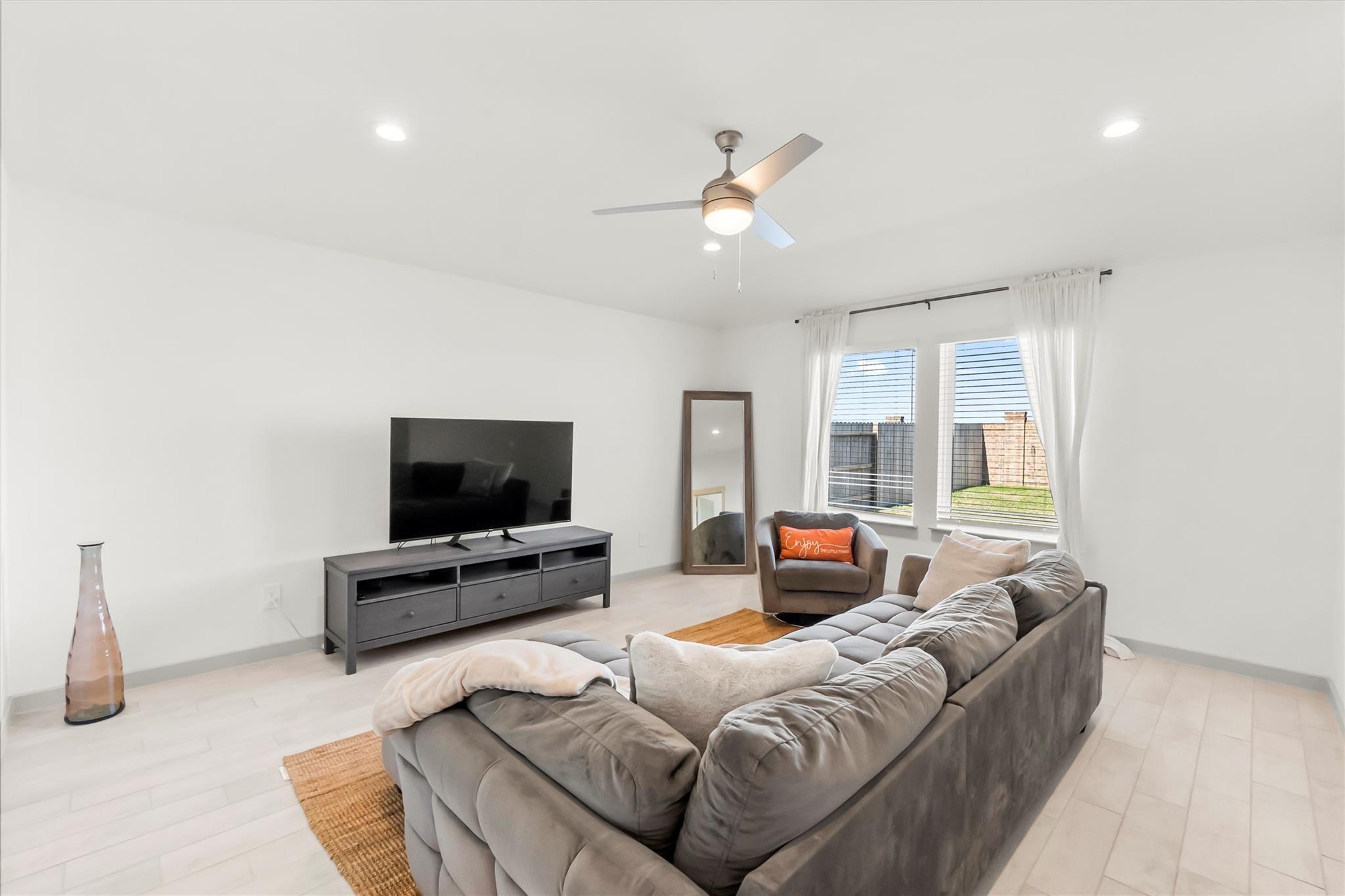 Furnished living room with a gray sectional, television, and two curtained windows.