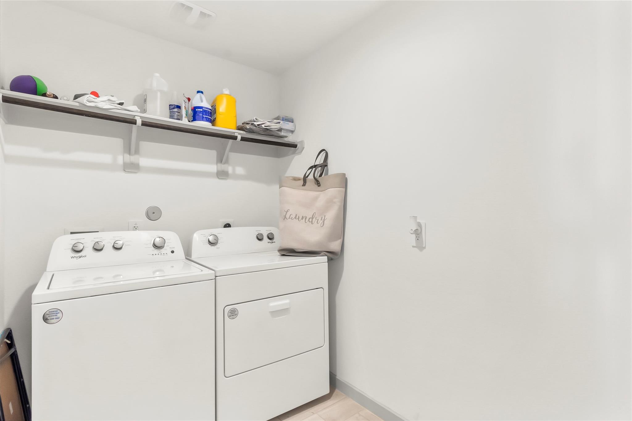Laundry room with a washer, dryer, and wall shelf stocked with cleaning supplies.