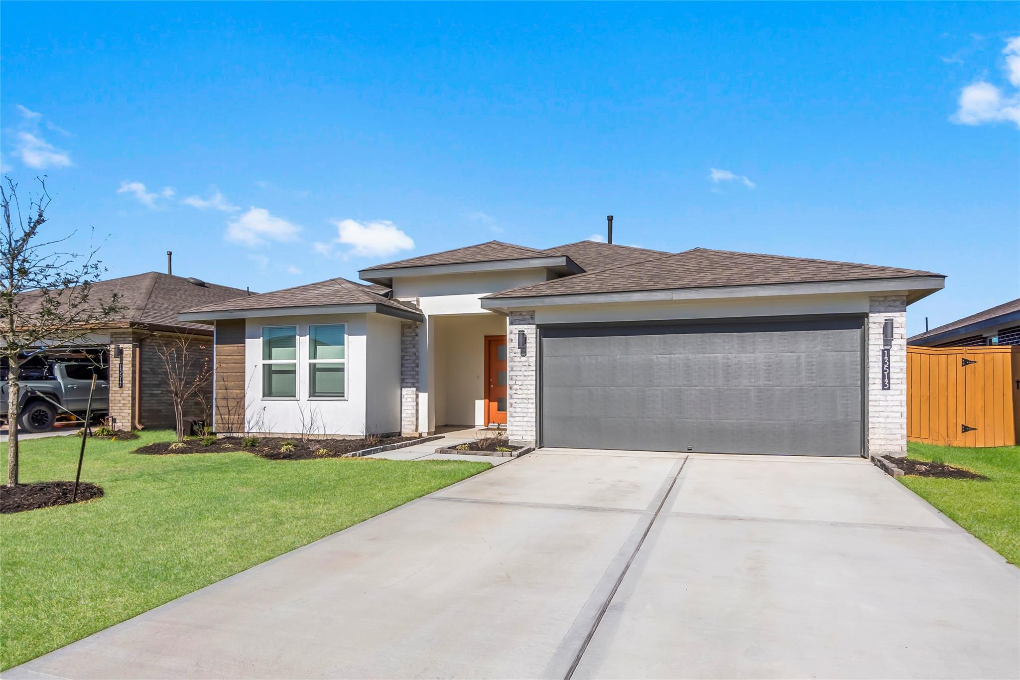 Modern single-story home with a wide gray garage door, orange entry door, and broad concrete driveway.