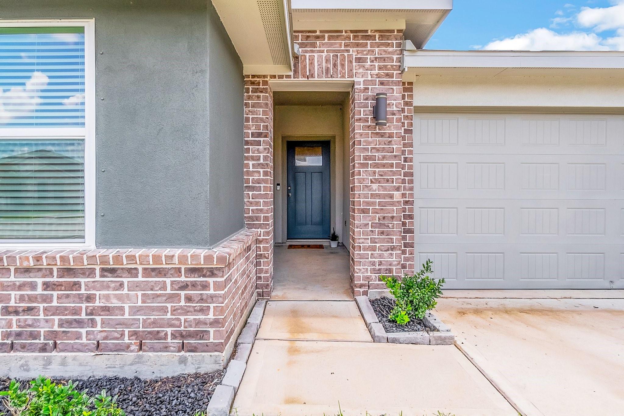 Recessed blue front door framed by red brick beside a white garage door.