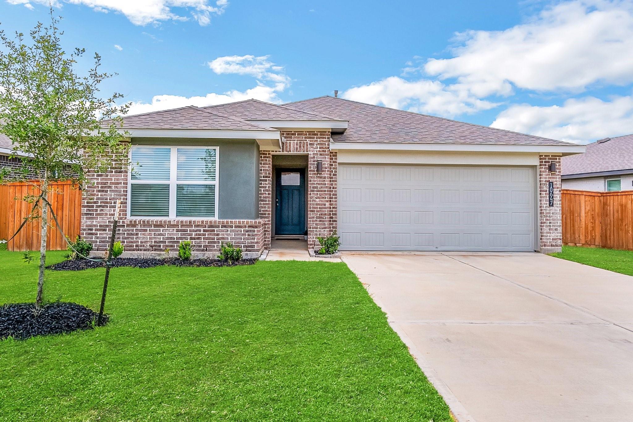 Single-story brick home with a blue front door, double garage, driveway, and broad green lawn.