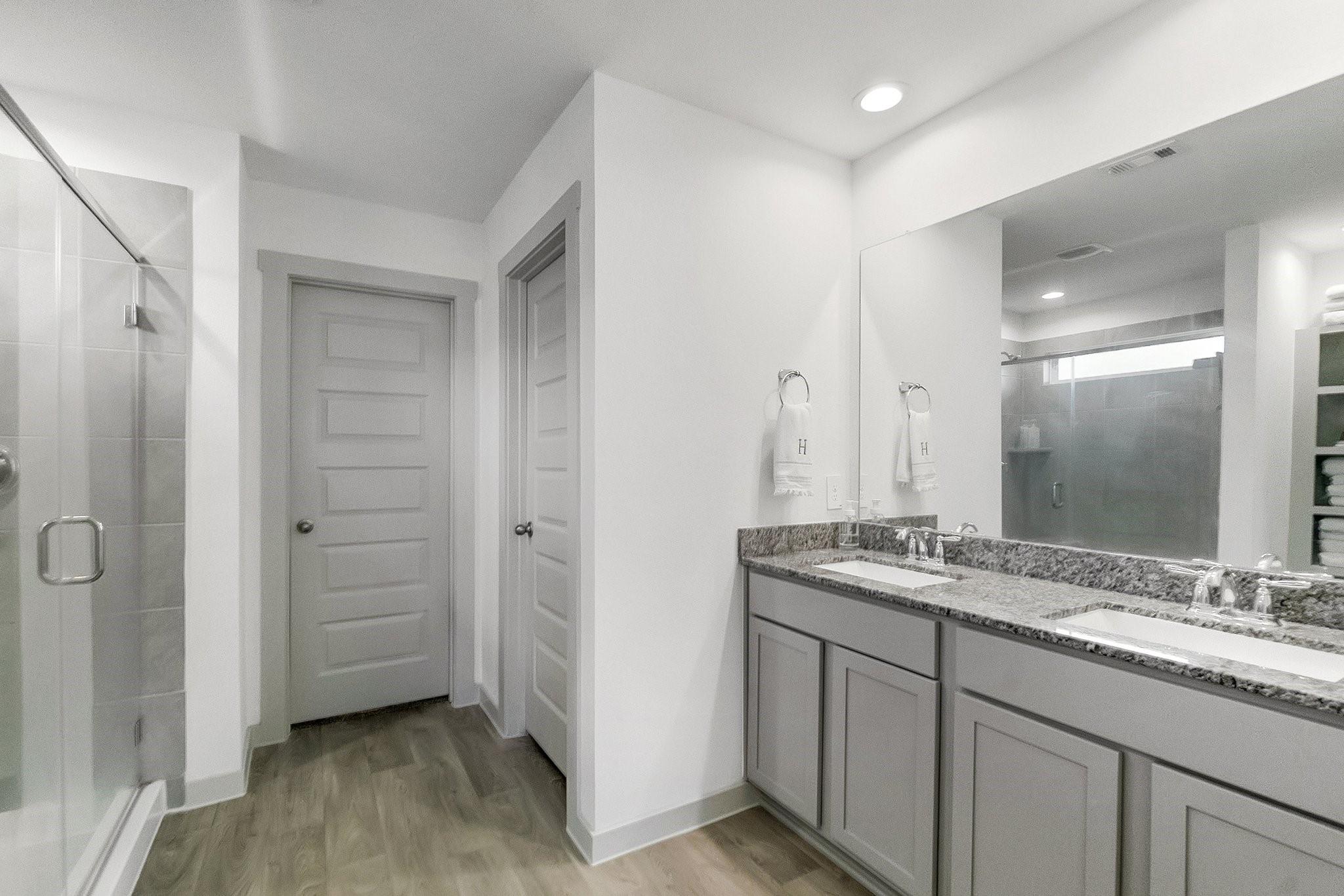 Bathroom with double vanity, granite countertop, large mirror, and glass-enclosed shower.
