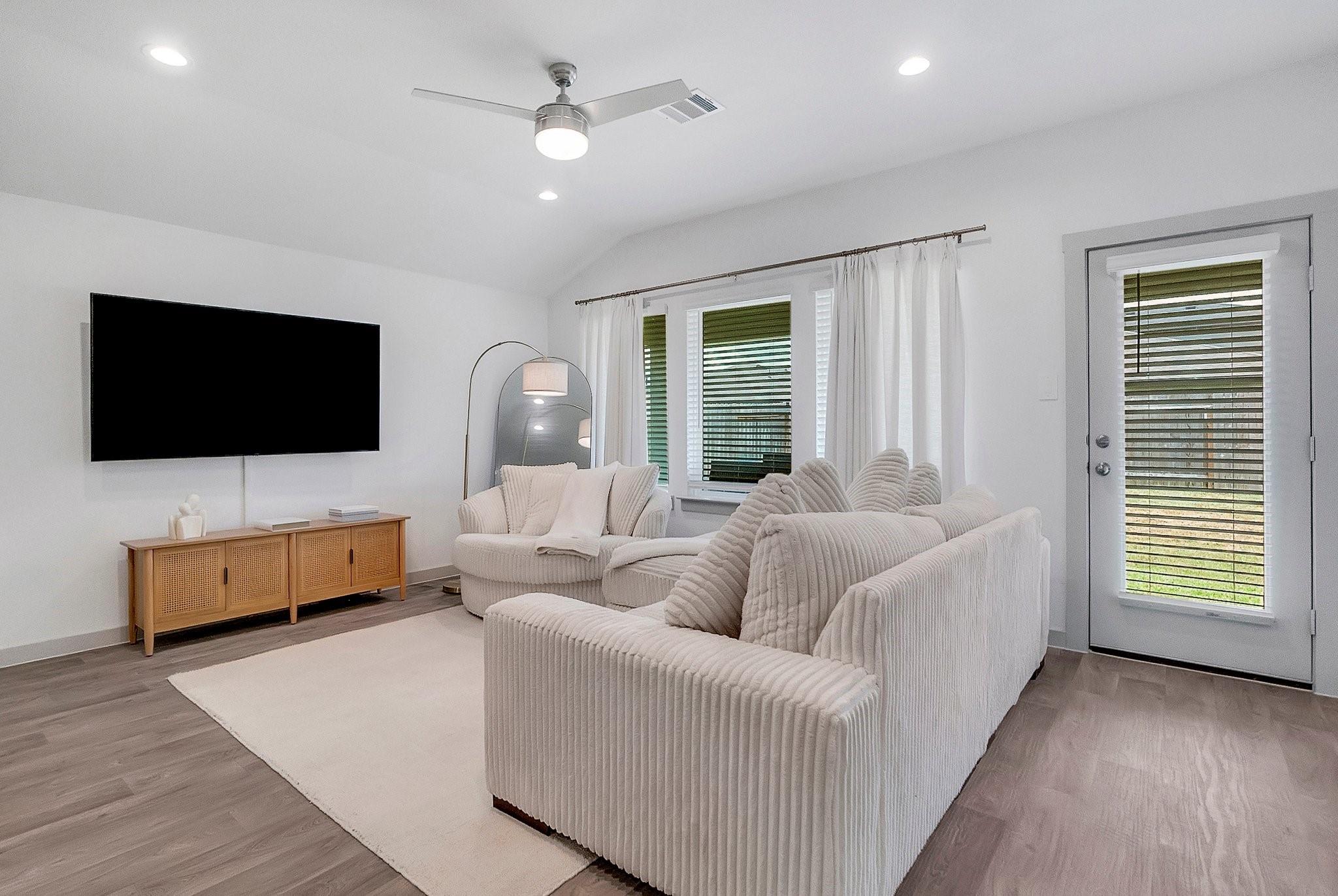 Furnished living room with white ribbed sofas, a wall-mounted TV, and a glass door with blinds.